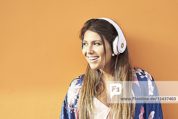 Portrait of smiling young woman with headphones in front of orange background