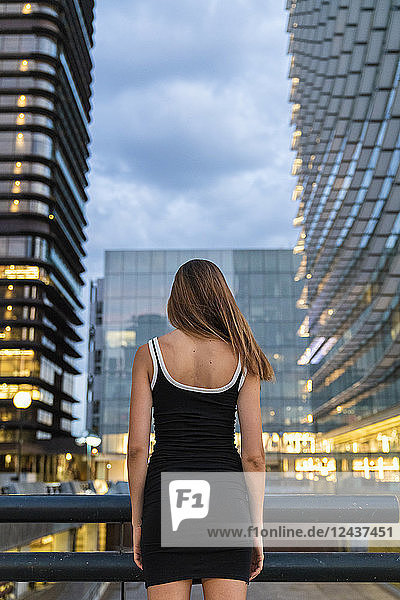 Rear view of young woman wearing black dress in the city at dusk