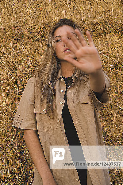 Young woman standing in front of hay bales making rejecting hand gesture  portrait