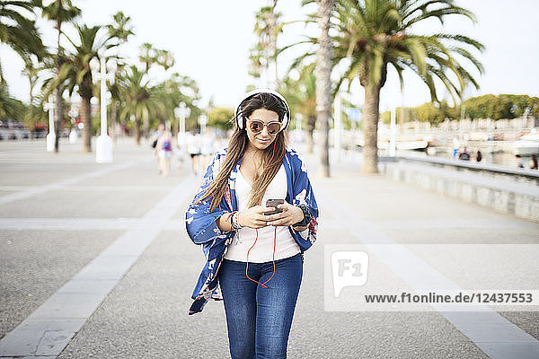 Portrait of woman wearing sunglasses listening music with headphones while looking at smartphone