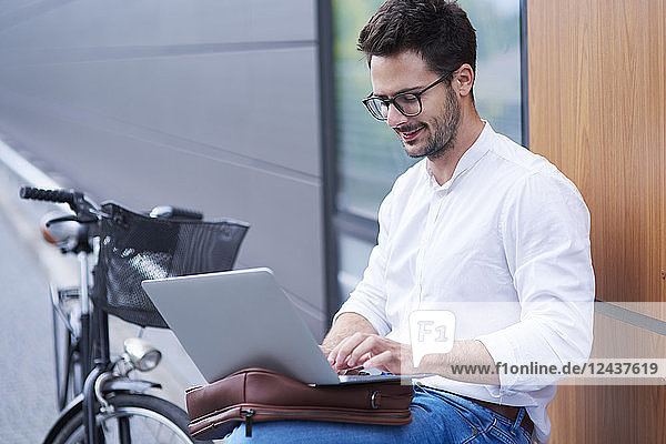 Businessman with bicycle using laptop outdoors