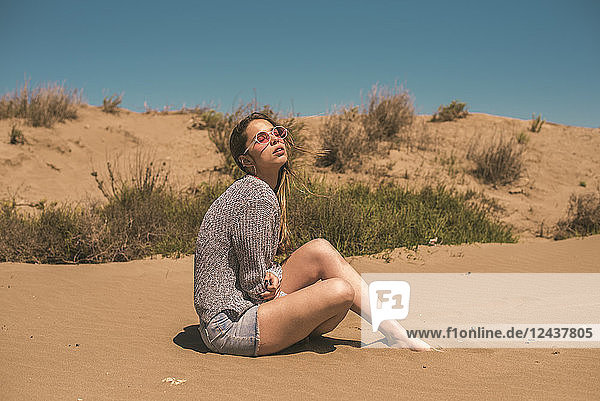 Spain  young woman wearing sunglasses sitting on the beach relaxing