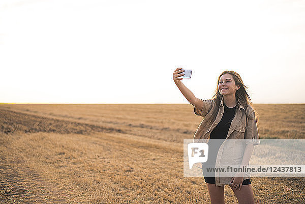 Young woman standing in field  making smartphone selfie