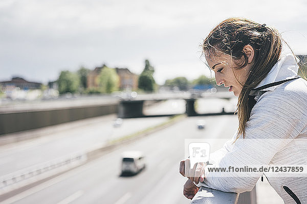 Sportive young woman looking on watch at motorway