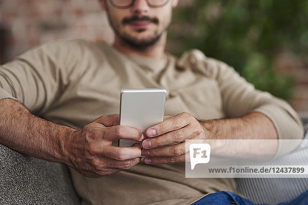 Man sitting on couch text messaging  partial view