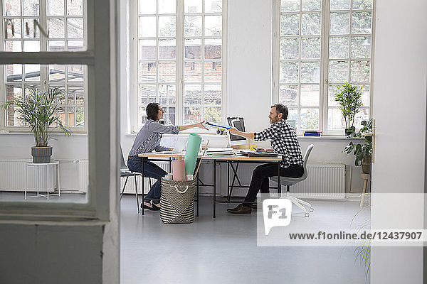 Man handing over folder to colleague at desk in a loft office