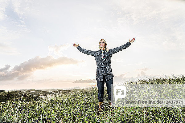 Happy woman standing in dunes with raised arms