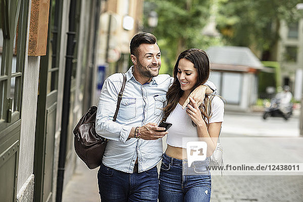 Smiling tourist couple with cell phone walking in the city