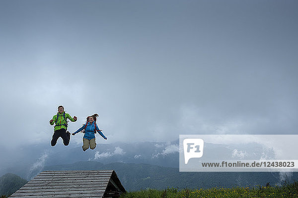 Germany  Brauneck  happy young hiker couple with backpacks jumping in the air