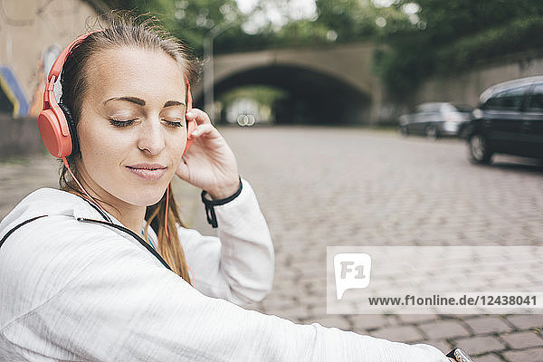 Smiling sportive young woman with closed eyes wearing headphones outdoors