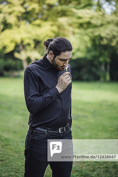 Young man  dressed in black  standing in park  smelling flower
