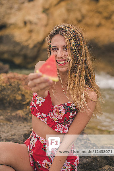 Portrait of happy young woman on rocks at the sea holding watermelon slice