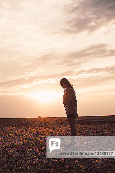 Lonely young woman standing on field at sunset