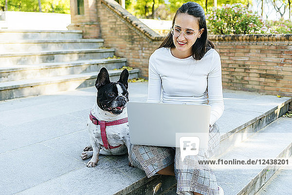 Woman using laptop next to her dog  sitting on stairs