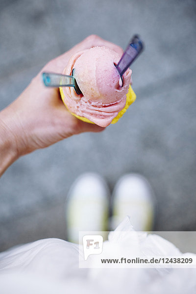 Woman's hand holding ice cream cone with two scoops and spoons