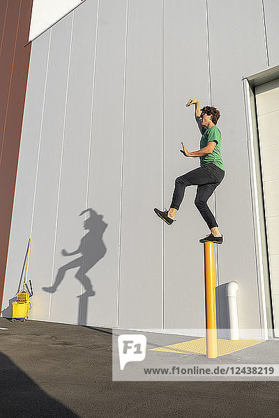 Acrobat standing on pole  casting shadow at cleaning bucket
