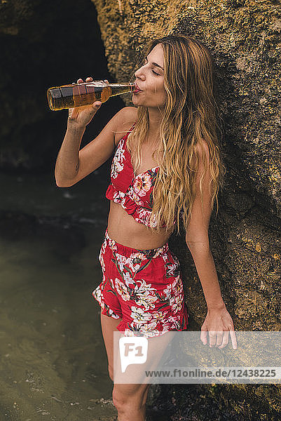 Young woman drinking a beer at a rock in the sea