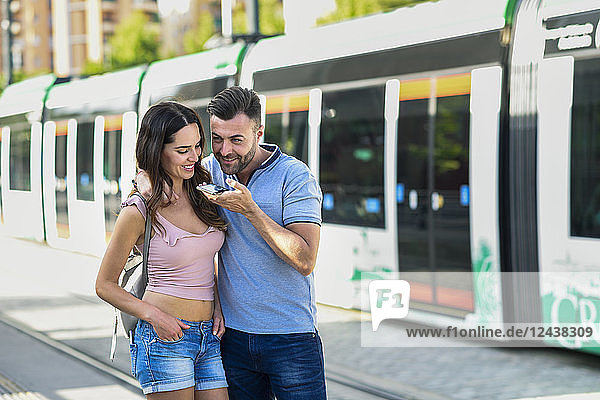 Couple using smartphone while waiting for tram at the station