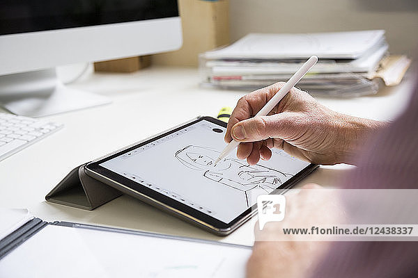Close-up of man working at desk in office drawing female figure on tablet