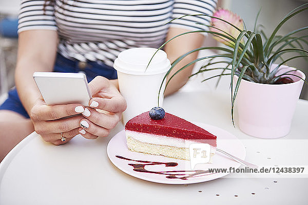 Close-up of woman using cell phone and eating cake at an cafe