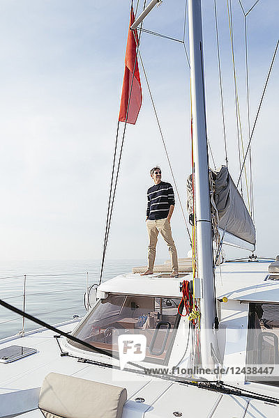 Mature man standing on a catamaran with hands in pockets,  smiling