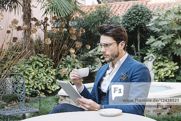 Elegant businessman using tablet in a garden cafe