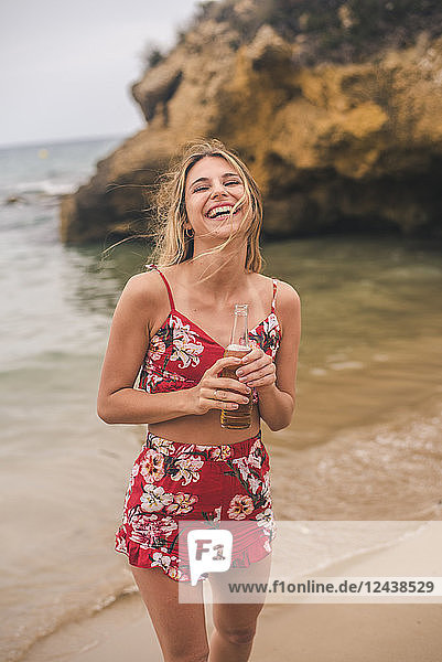 Portrait of happy young woman standing with a beer on the beach