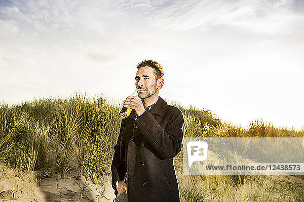 Smiling woman drinking a beer in dunes
