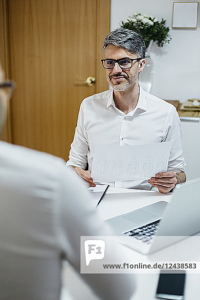 Smiling man at desk holding paper looking at colleague