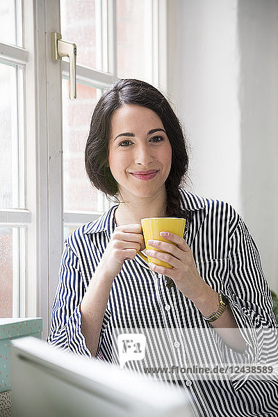 Portrait of smiling woman with cup of coffee at the window in office