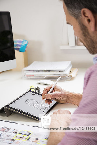 Man working at desk in office drawing female figure on tablet