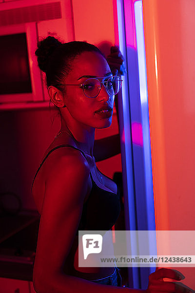 Portrait of beautiful young woman wearing bra and glasses in a dark illuminated room