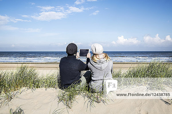 Couple sitting in dunes on the beach with tablet