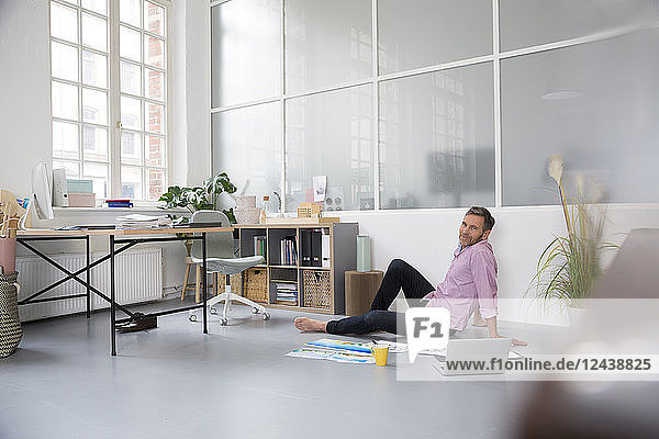 Casual man with plans and laptop sitting on the floor in a loft office