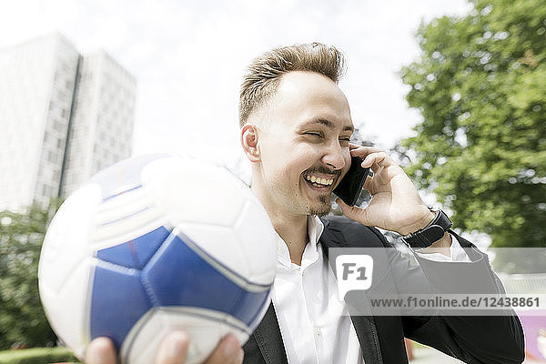 Happy young businessman with football talking on cell phone in the city