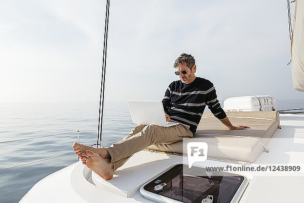 Mature man sitting on deck of a catamaran  using laptop