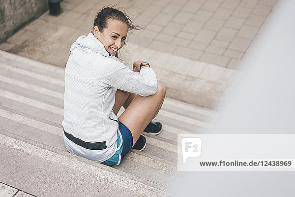 Smiling sportive young woman sitting on stairs outdoors