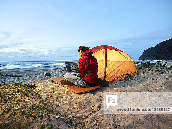 USA  Hawaii  Kauai  Polihale State Park  woman using laptop at tent on the beach at dusk