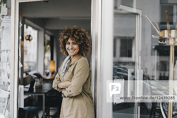 Smiling woman standing with arms crossed in door of coworking space