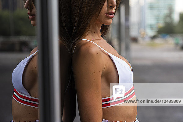 Close-up of attractive young woman in sportswear leaning against glass front of a building