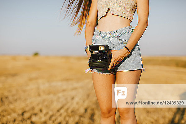 Young woman with instant camera on a field at sunset partial view
