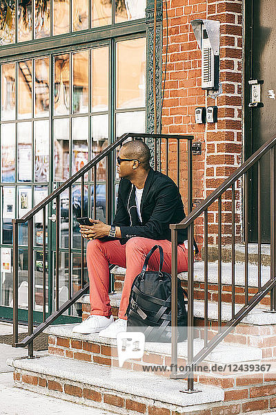 USA  NYC  Brooklyn  Man waiting on stairs  using smartphone