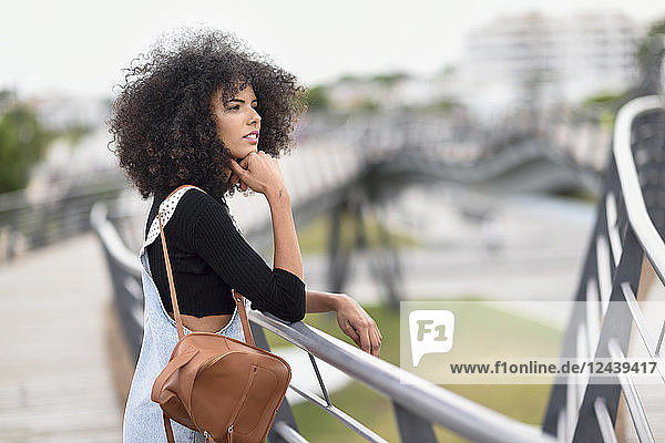 Young woman with brown leather backpack standing on a bridge looking at distance