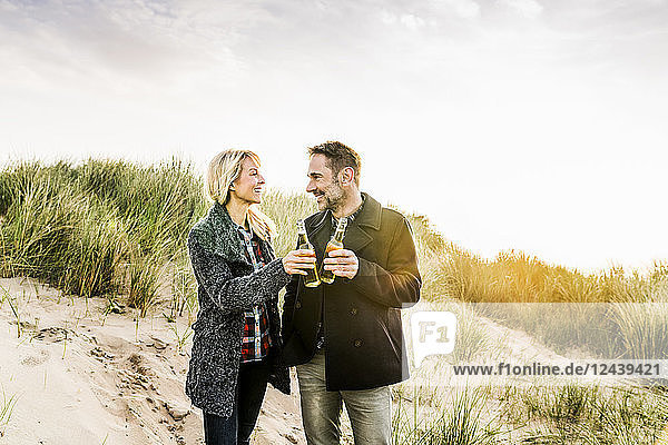 Happy couple in dunes clinking beer bottles