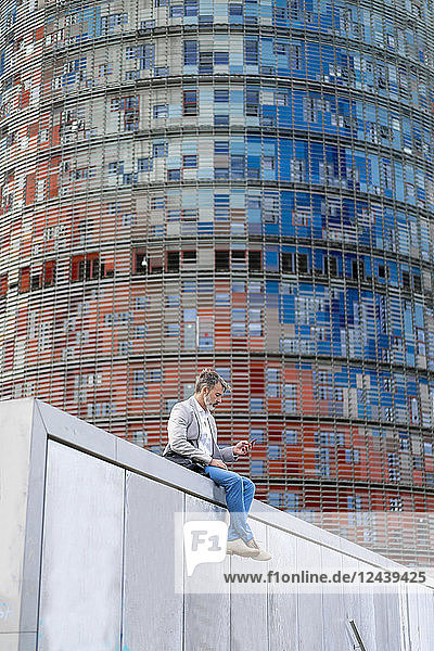 Spain  Barcelona  businessman sitting on wall using cell phone