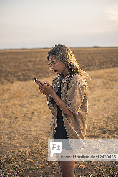 Young woman standing in field  using smartphone