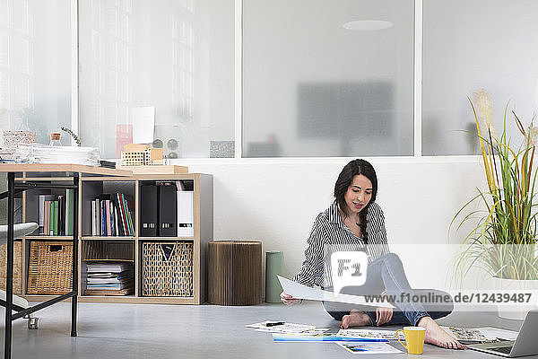 Casual woman with plans and laptop sitting on the floor in a loft office