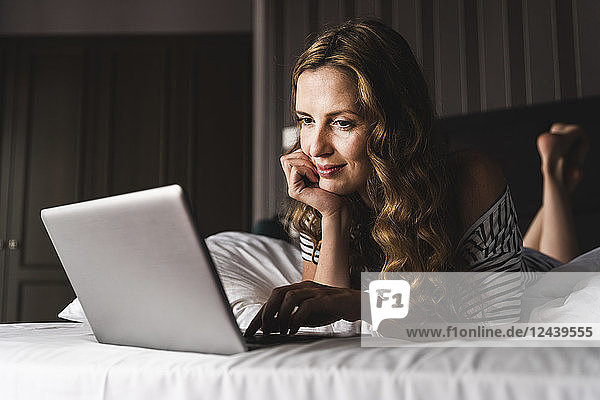 Smiling woman lying on bed at home looking at laptop
