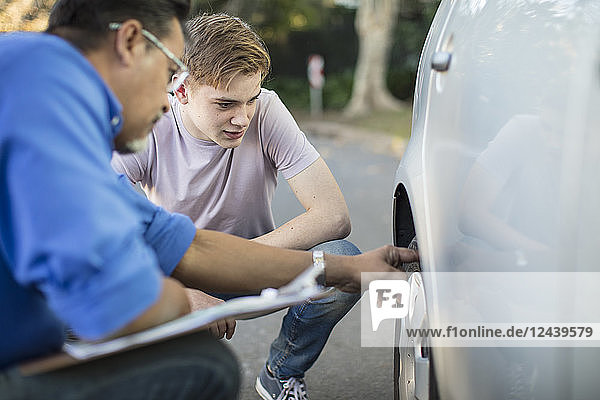 Learner driver with instructor checking tyre of a car