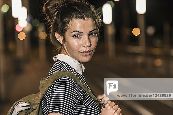 Portrait of young woman with backpack waiting at station by night